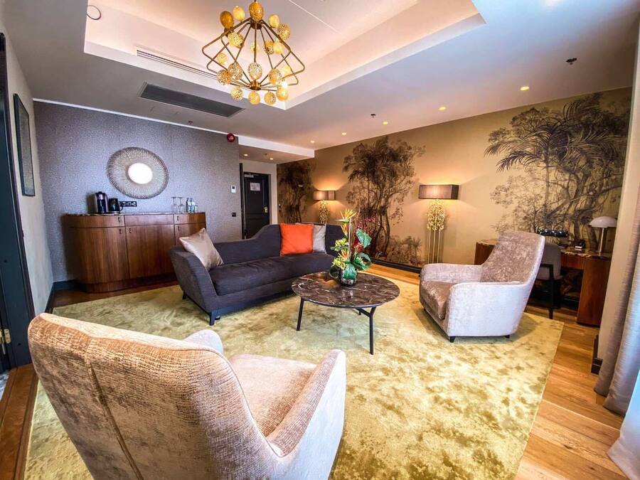 A modern living room with a dark sofa, two armchairs, a coffee table, and a decorative plant.