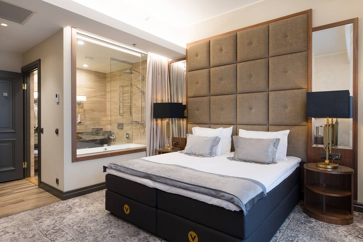 A modern bedroom with a large bed, a glass shower, and a vanity with a mirror.