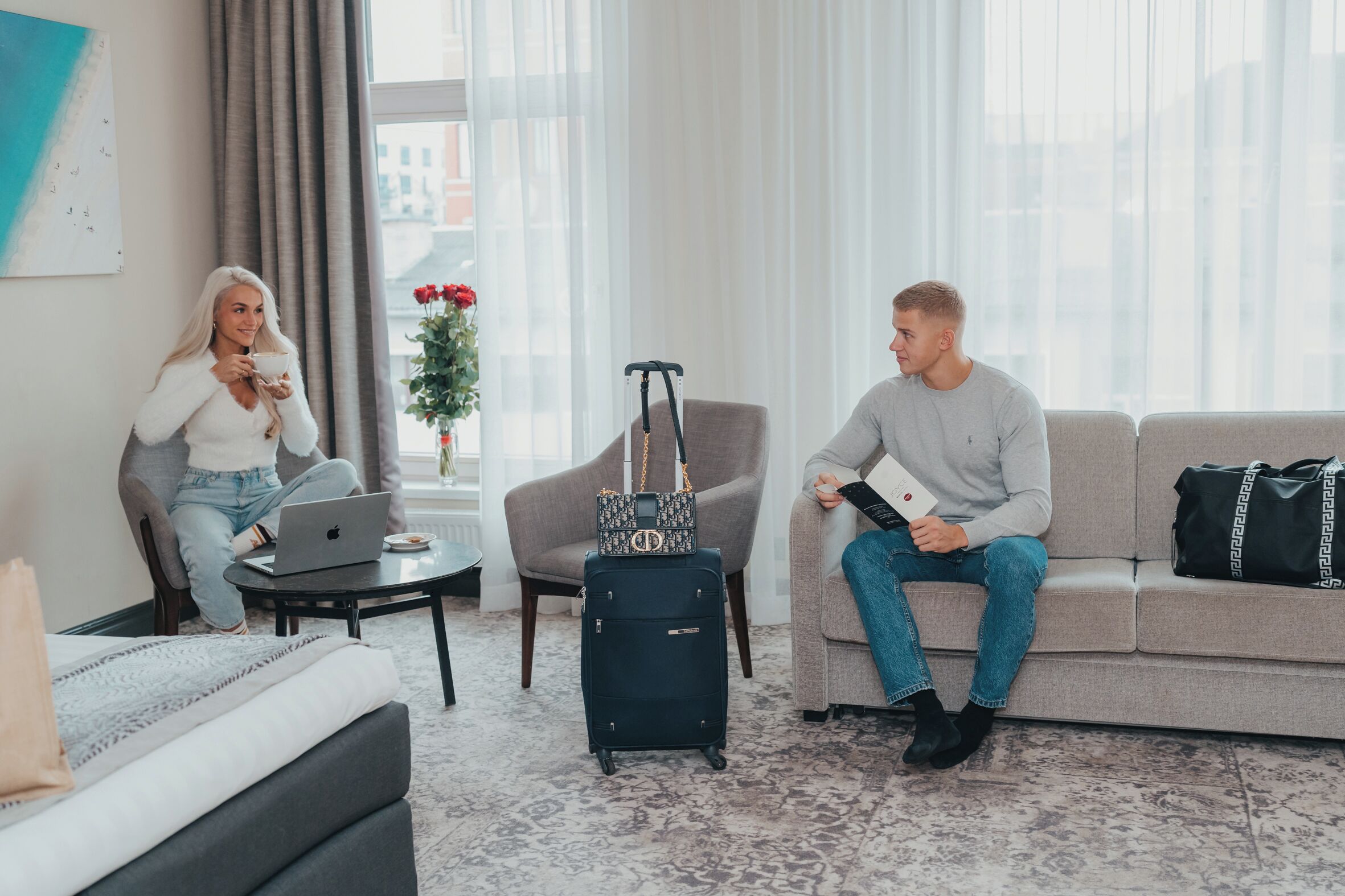 A living room with a sofa, a coffee table, a laptop, a suitcase, and a handbag.
