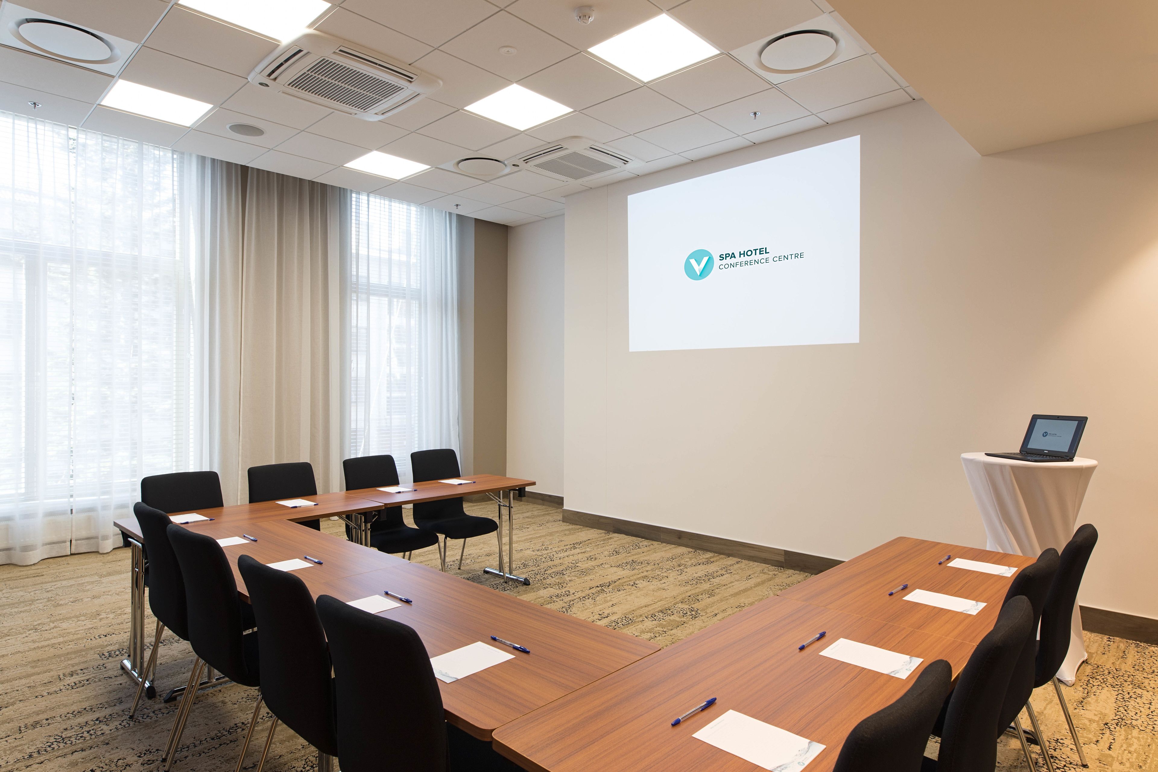 A conference room with a long table, black chairs, a projector screen, and a laptop on a small table.