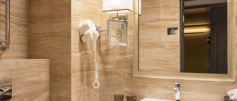 A modern bathroom with a marble wall, a large mirror, a sink, a hairdryer, and neatly folded towels.