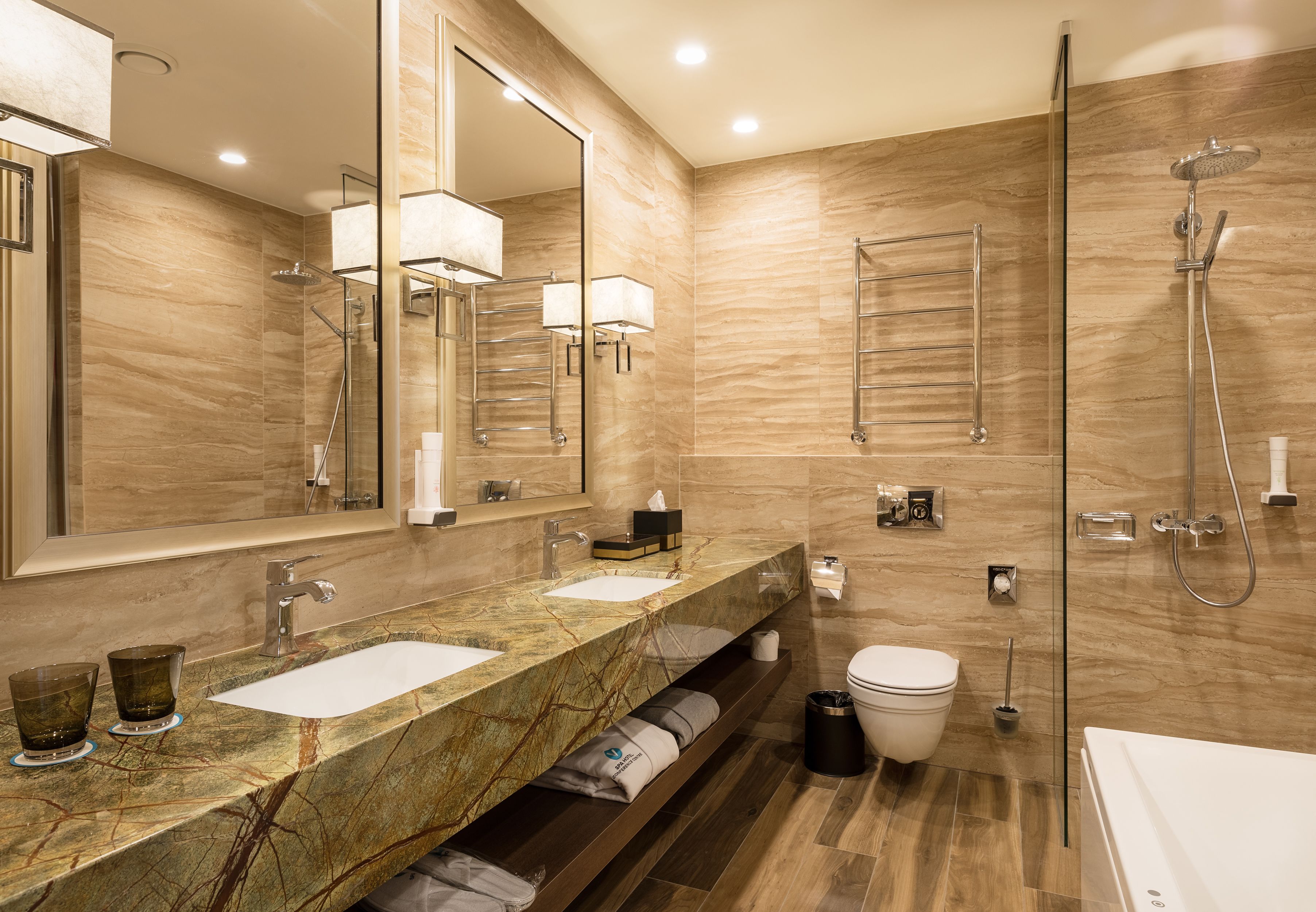A modern bathroom with two sinks, a large mirror, a shower, and a toilet.