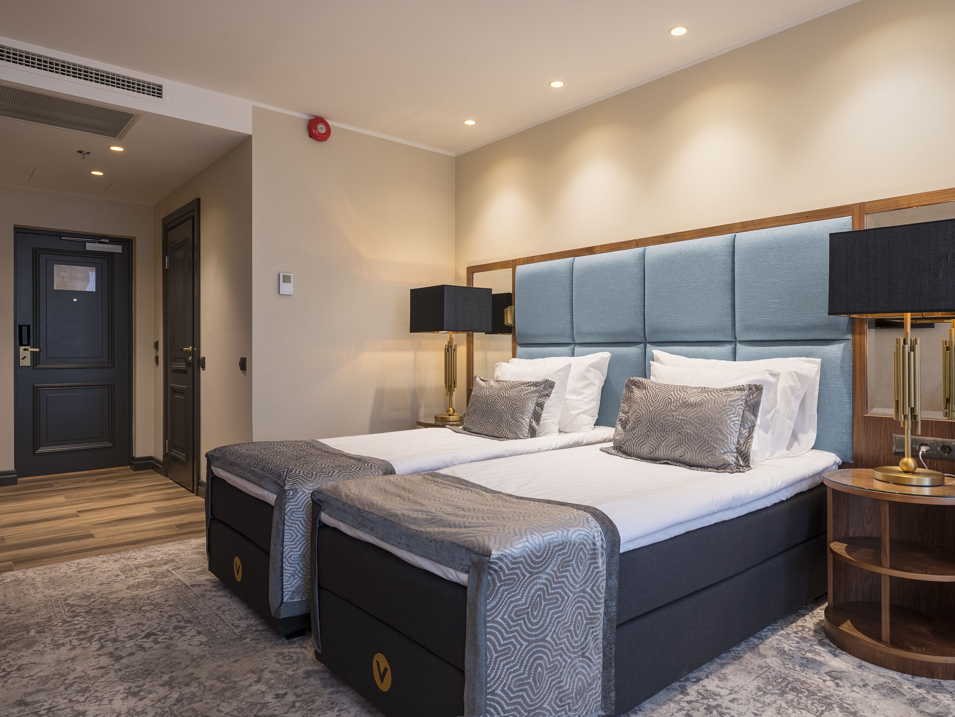 Une chambre d’hôtel avec un lit double, deux tables de chevet, une commode, une lampe et une porte avec une serrure.