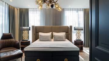 A modern hotel room with a large bed, a leather armchair, and a chandelier.