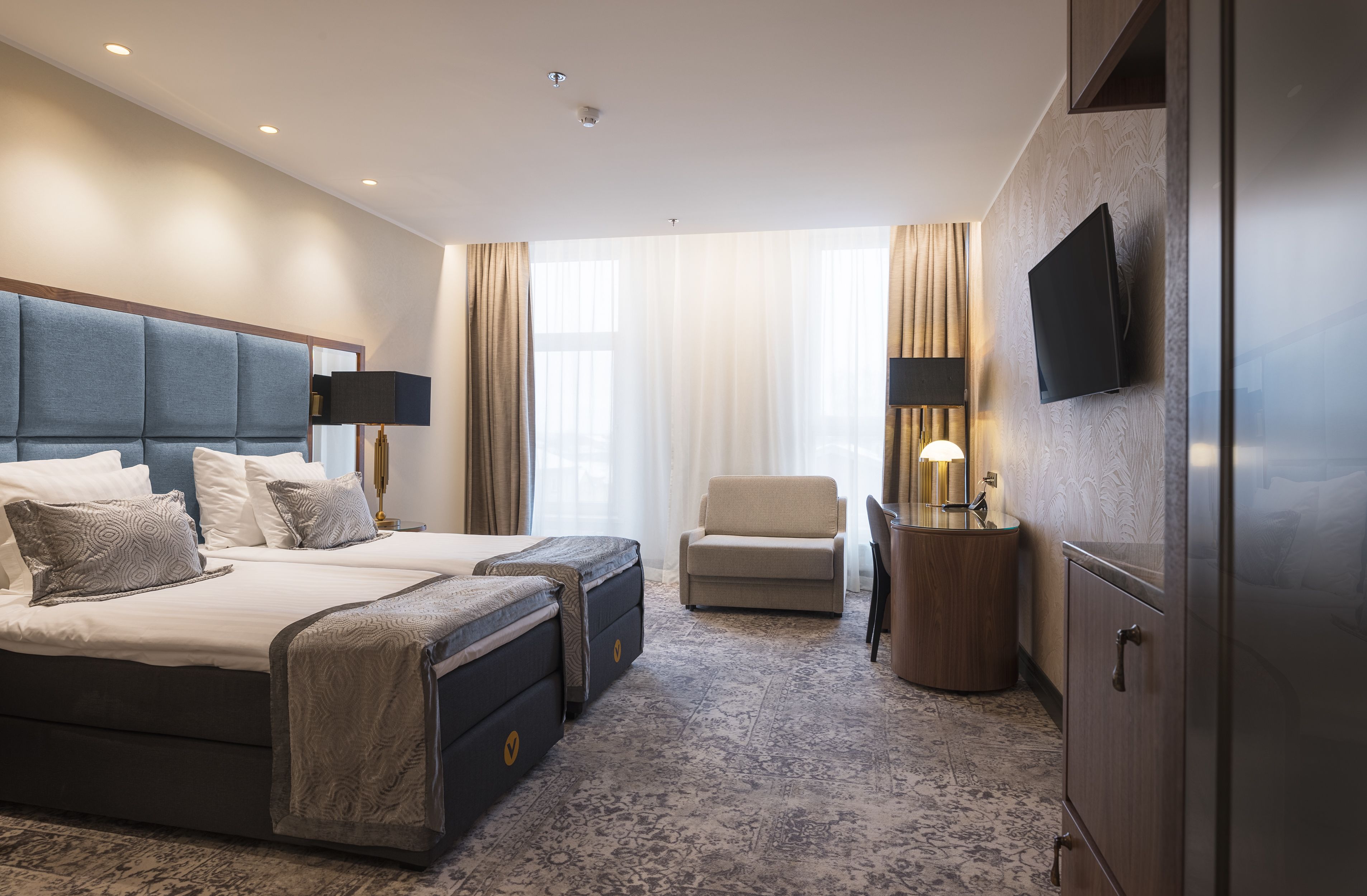 Habitación de hotel con una cama grande, un escritorio con lámpara, un televisor montado en la pared y un armario.