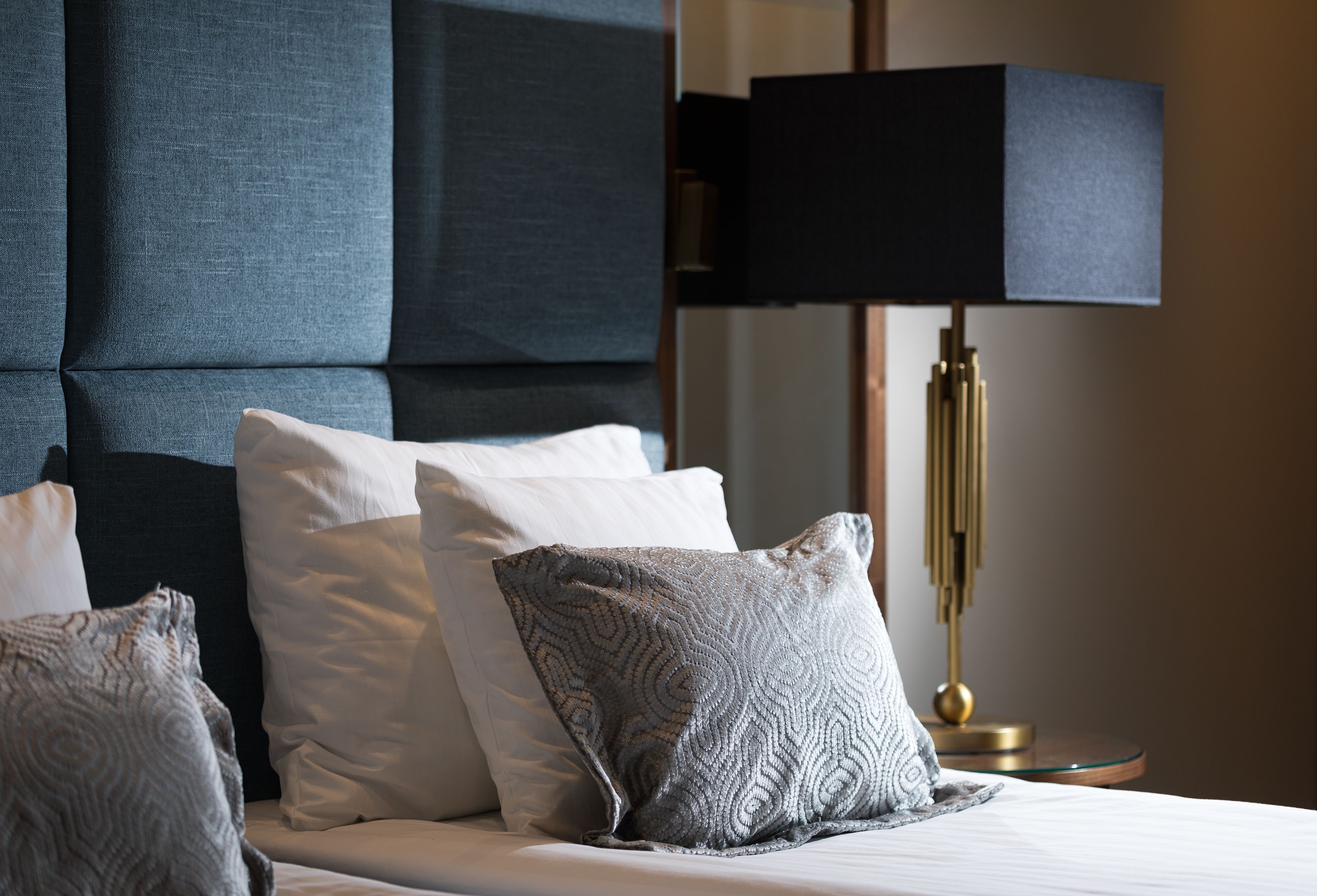 Una cama con varias almohadas, un cabecero oscuro y una lámpara de noche.