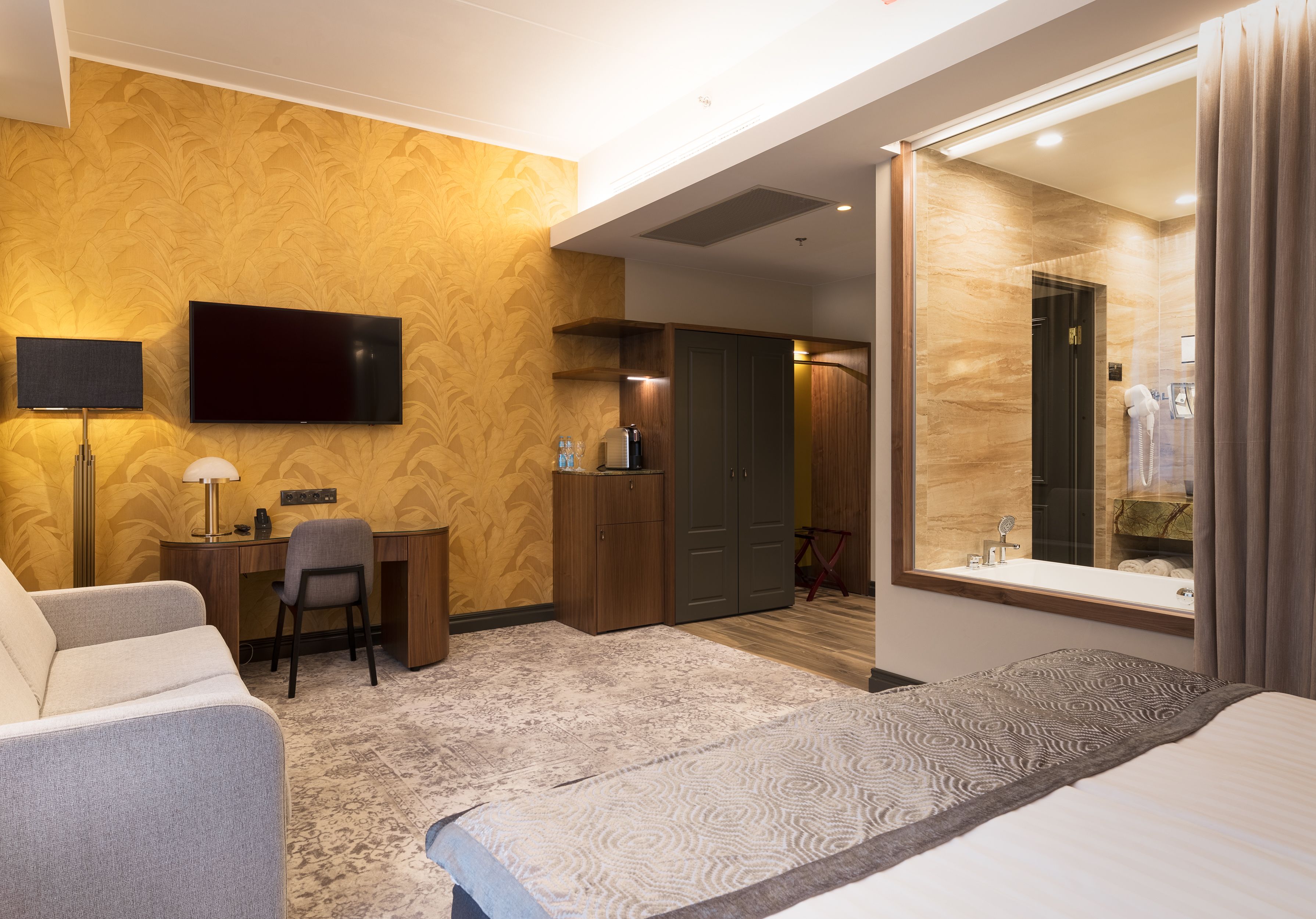 Ein Hotelzimmer mit Bett, Schreibtisch, Stuhl, Fernseher und einem durch eine Glastür einsehbaren Badezimmer.