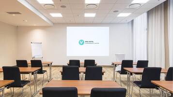 A conference room with a projector screen displaying the SPA HOTEL logo, arranged tables and chairs, and a whiteboard.