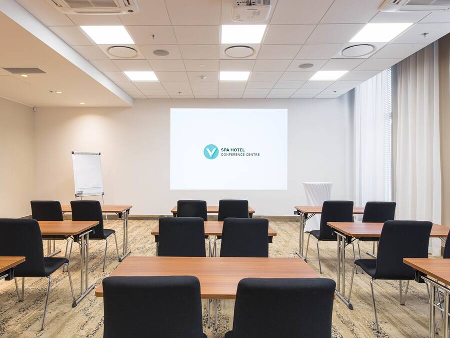 A conference room with a projector screen displaying the SPA HOTEL logo, arranged tables and chairs, and a whiteboard.