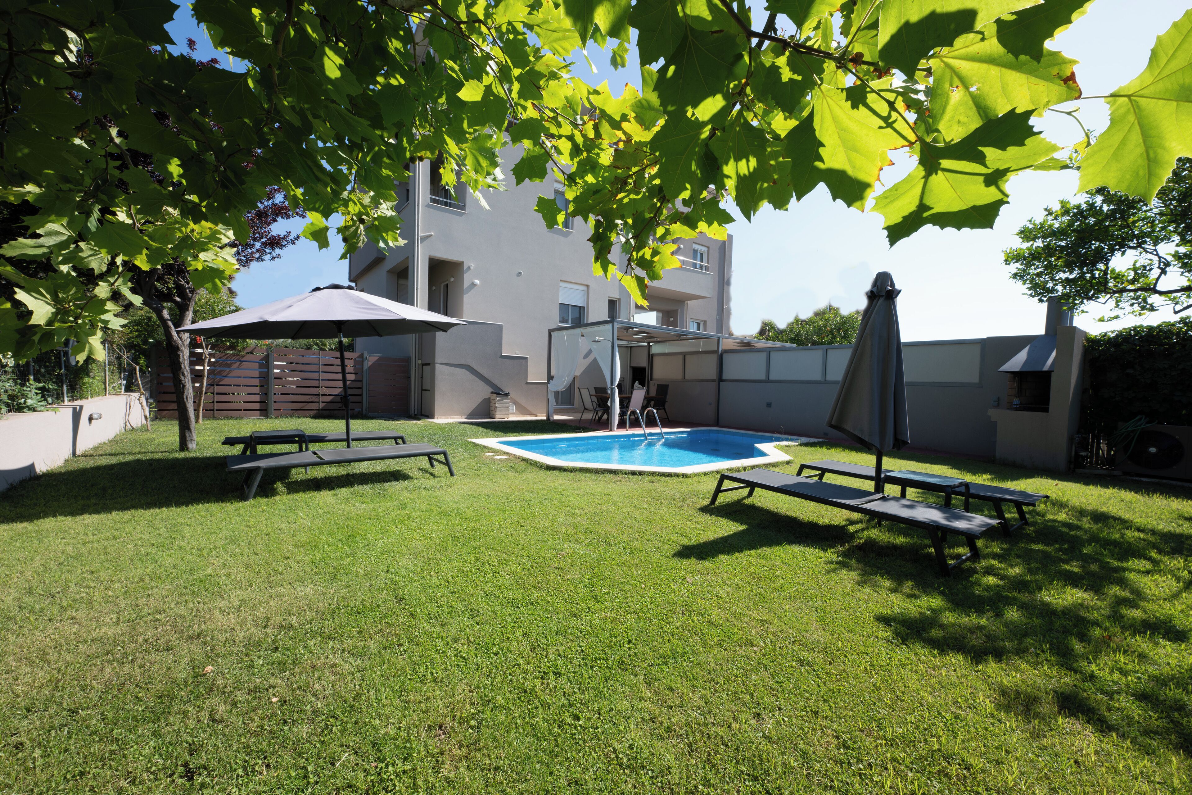 A backyard with a swimming pool, picnic tables, and a covered umbrella.