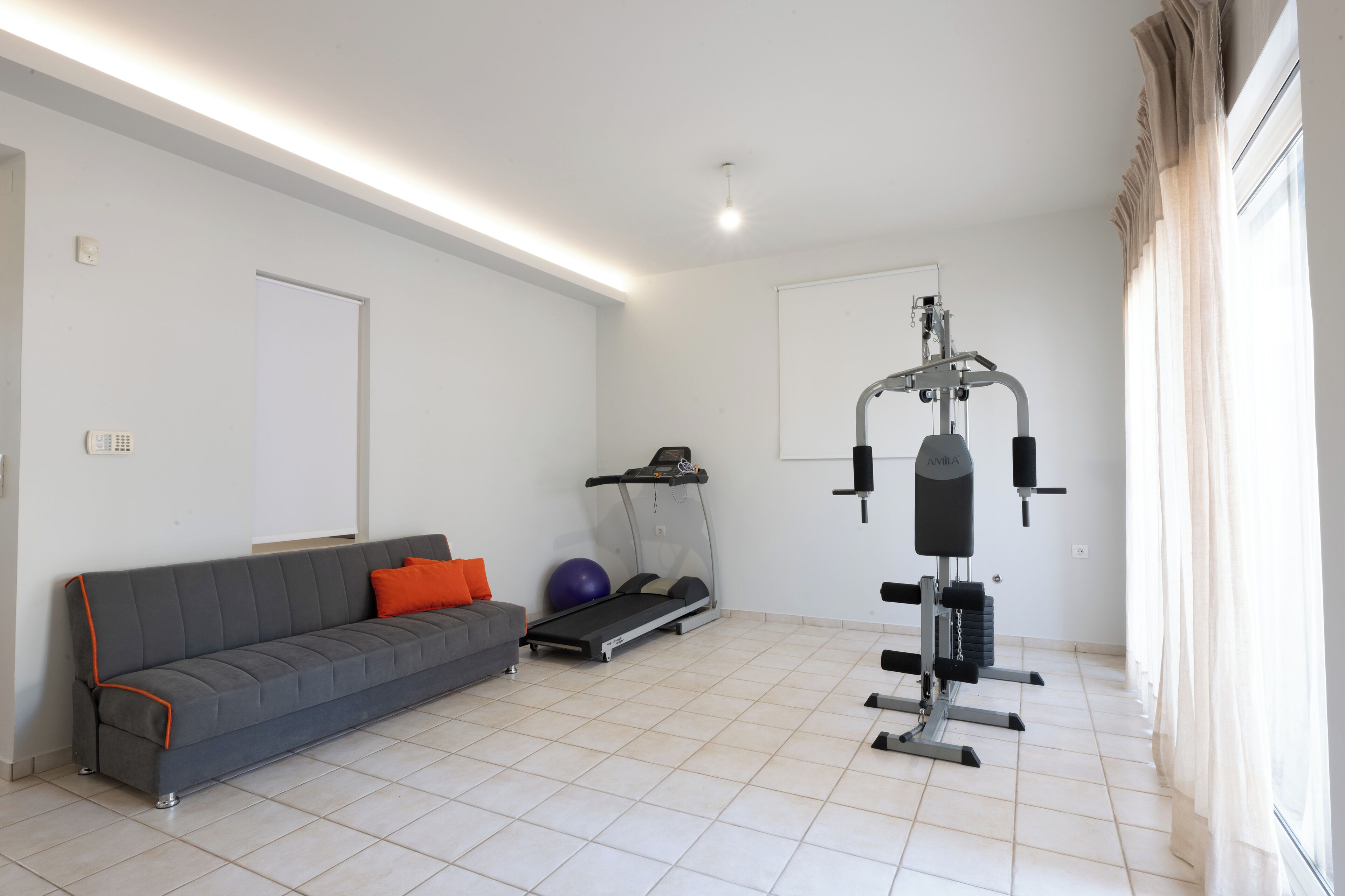 A modern living room with a grey sofa, exercise equipment, and a treadmill.