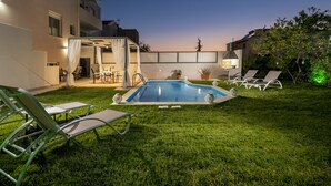 A backyard with a swimming pool, lounge chairs, and a covered patio area. - Dream Villa (Chania)