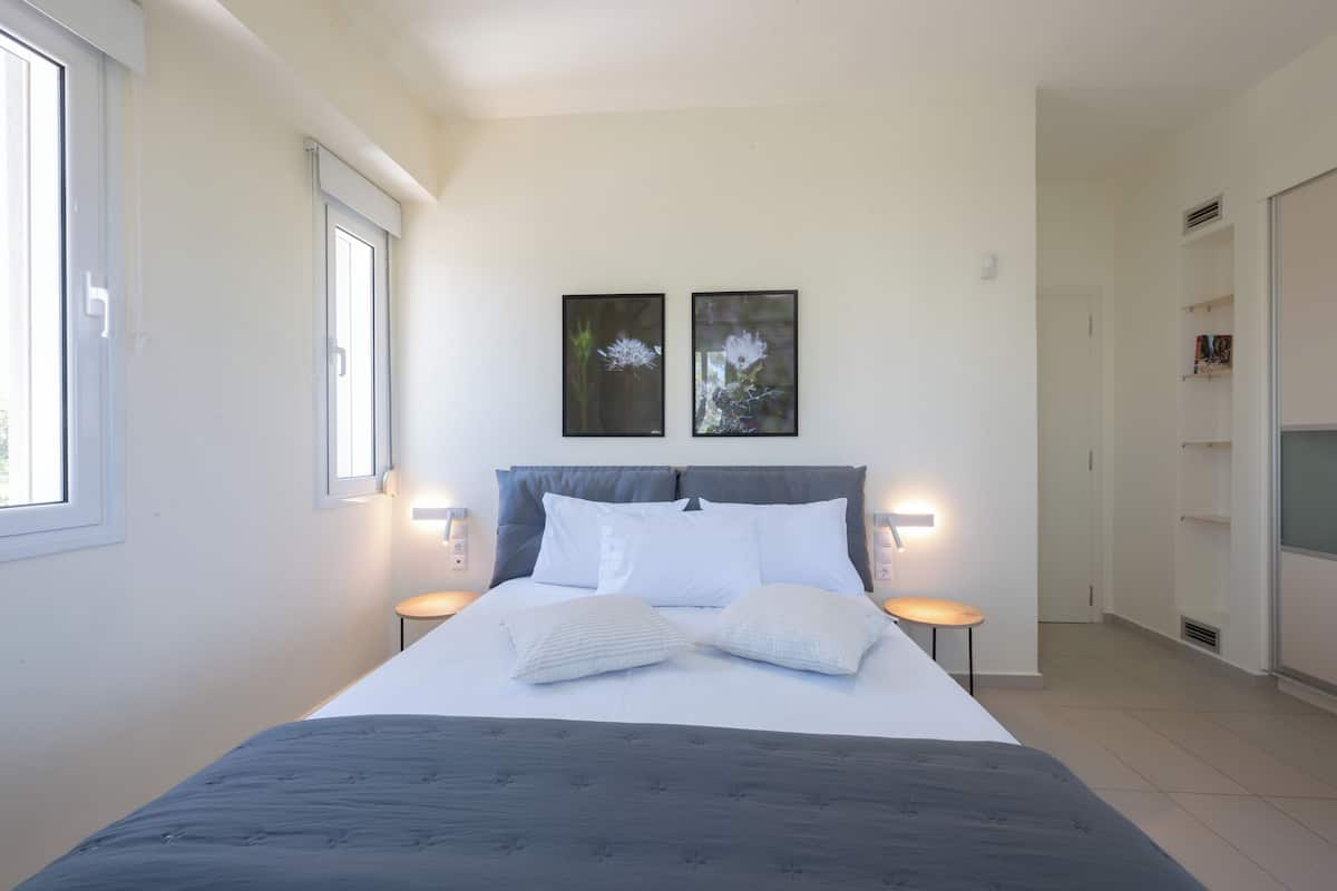 A modern bedroom with a large bed, two wall-mounted picture frames, bedside lamps, and a wardrobe.