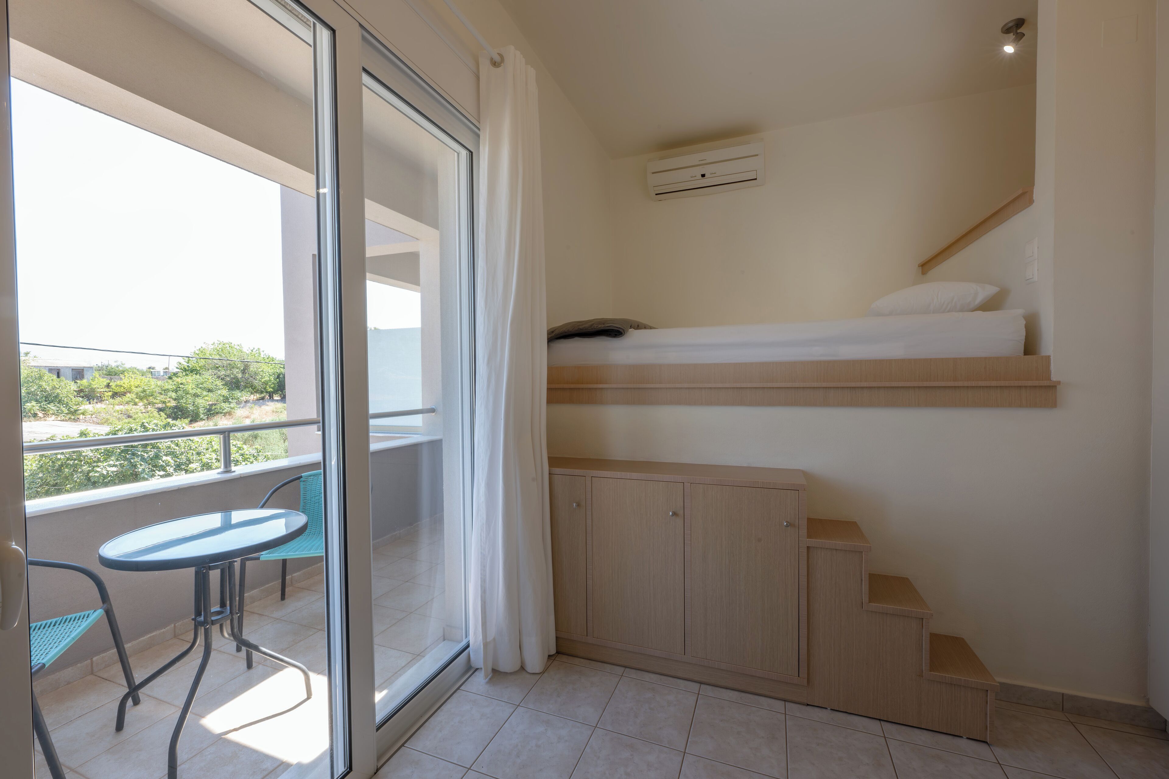 A balcony with a glass door, a small table, and a bed with a headboard.