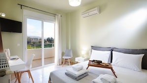 A hotel room with a bed, a table with towels, a chair, a TV, and a balcony with a view. - Dream Villa (Chania)