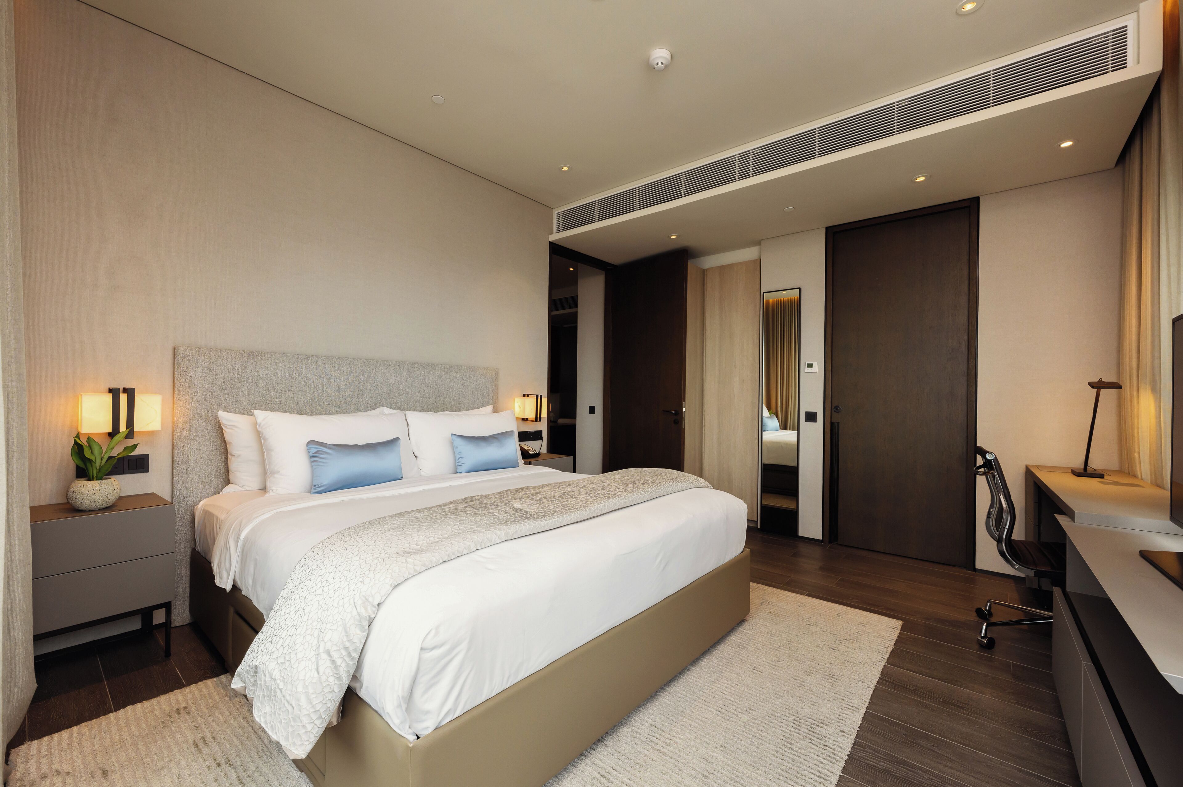 A modern bedroom with a large bed, bedside tables, a desk, and a chair.