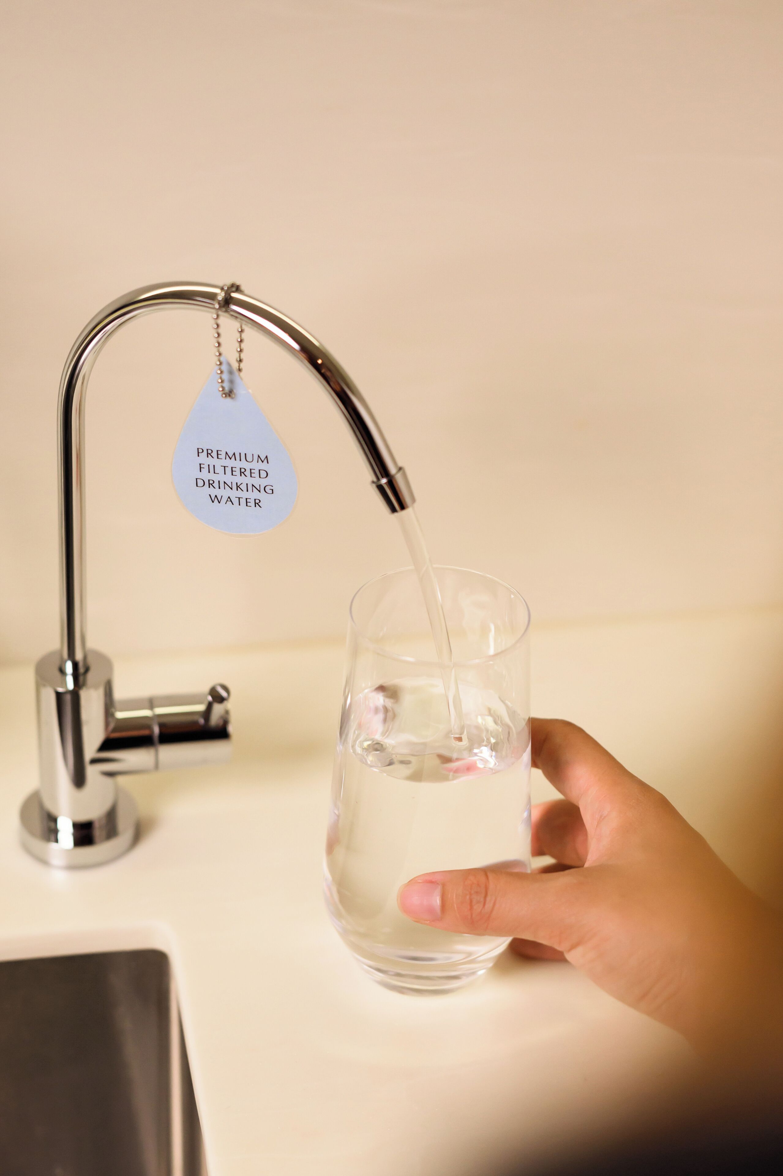 A hand holding a glass under a faucet with a label reading "Premium Filtered Drinking Water".
