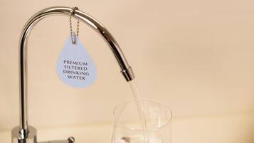 A hand holding a glass under a faucet with a label reading "Premium Filtered Drinking Water".