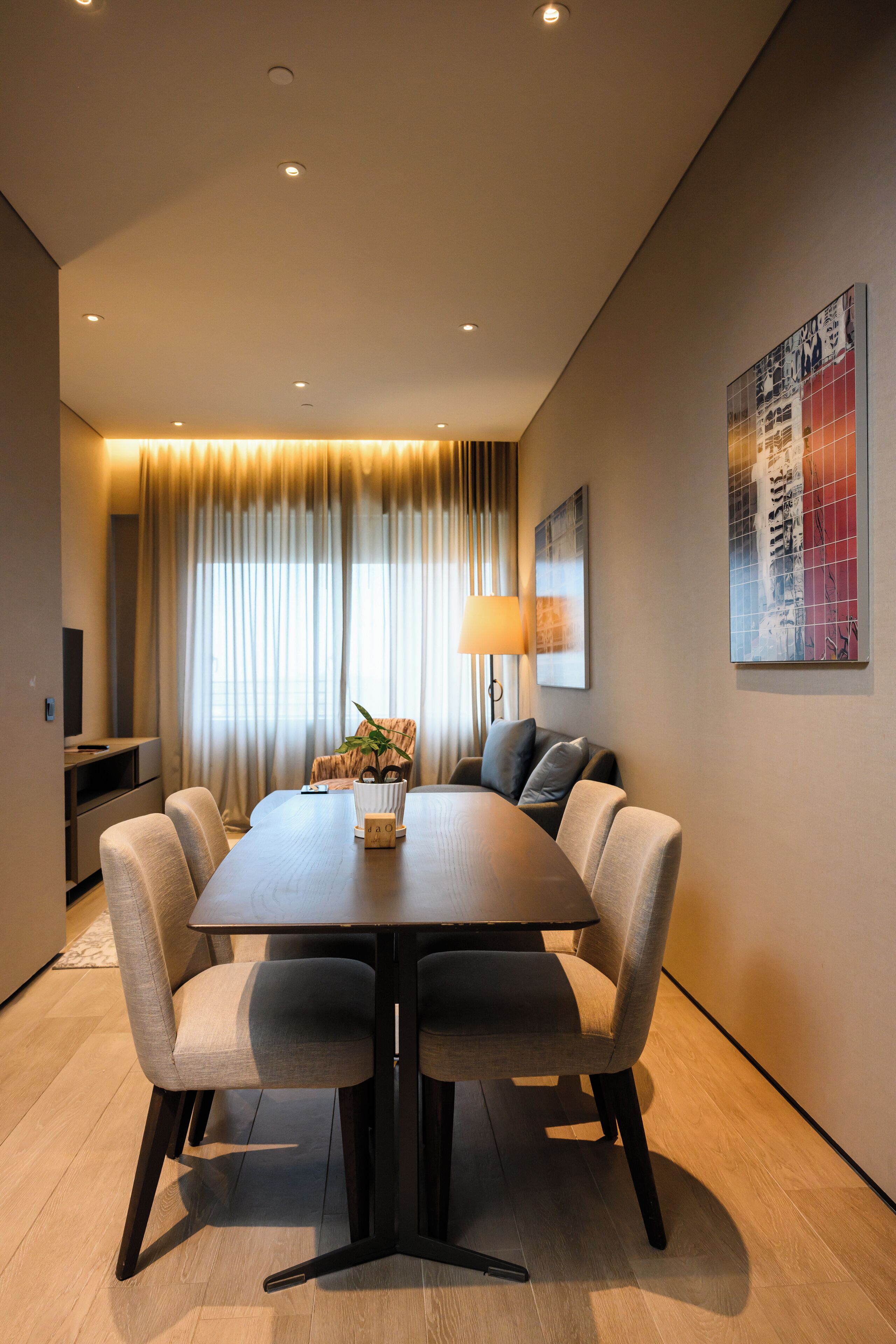 A modern dining area with a rectangular table, six chairs, a lamp, and a television on a stand.
