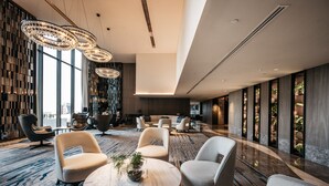 Un vestíbulo moderno con techos altos, ventanas amplias y una variedad de zonas de estar, incluyendo sofás y sillones.