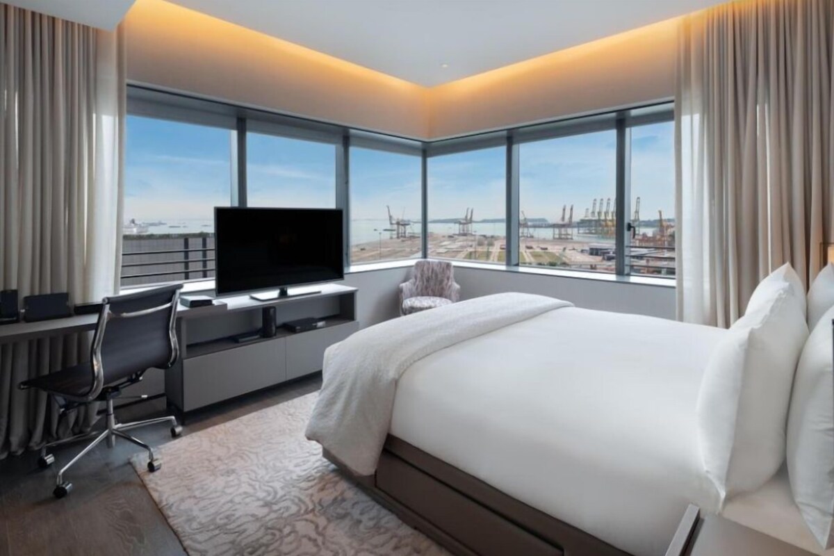A modern hotel room with a large bed, a desk with a computer, and a TV.