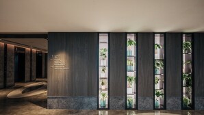 Un vestíbulo moderno con piso de mármol, paneles de madera oscura y estanterías verticales con plantas en macetas.