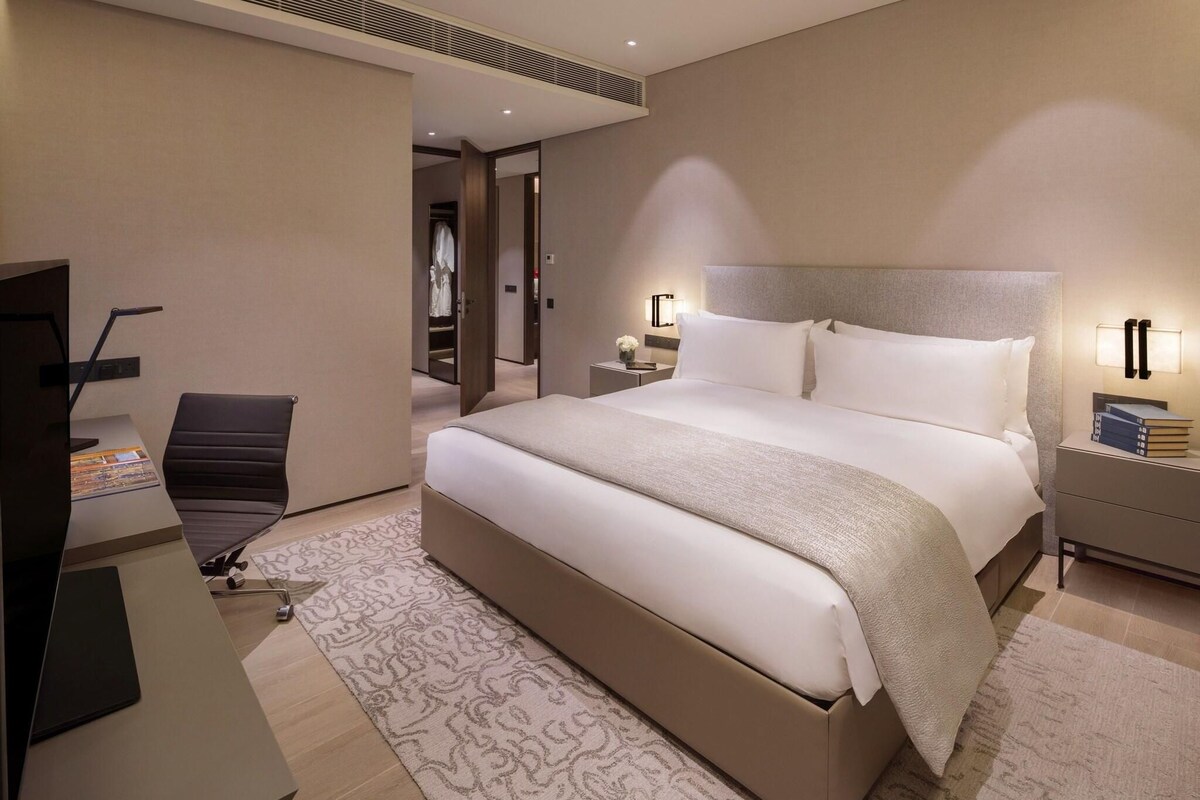 Ein modernes Hotelzimmer mit einem großen Bett, einem Schreibtisch mit Stuhl, einem Fernseher und einem Nachttisch mit Lampe.