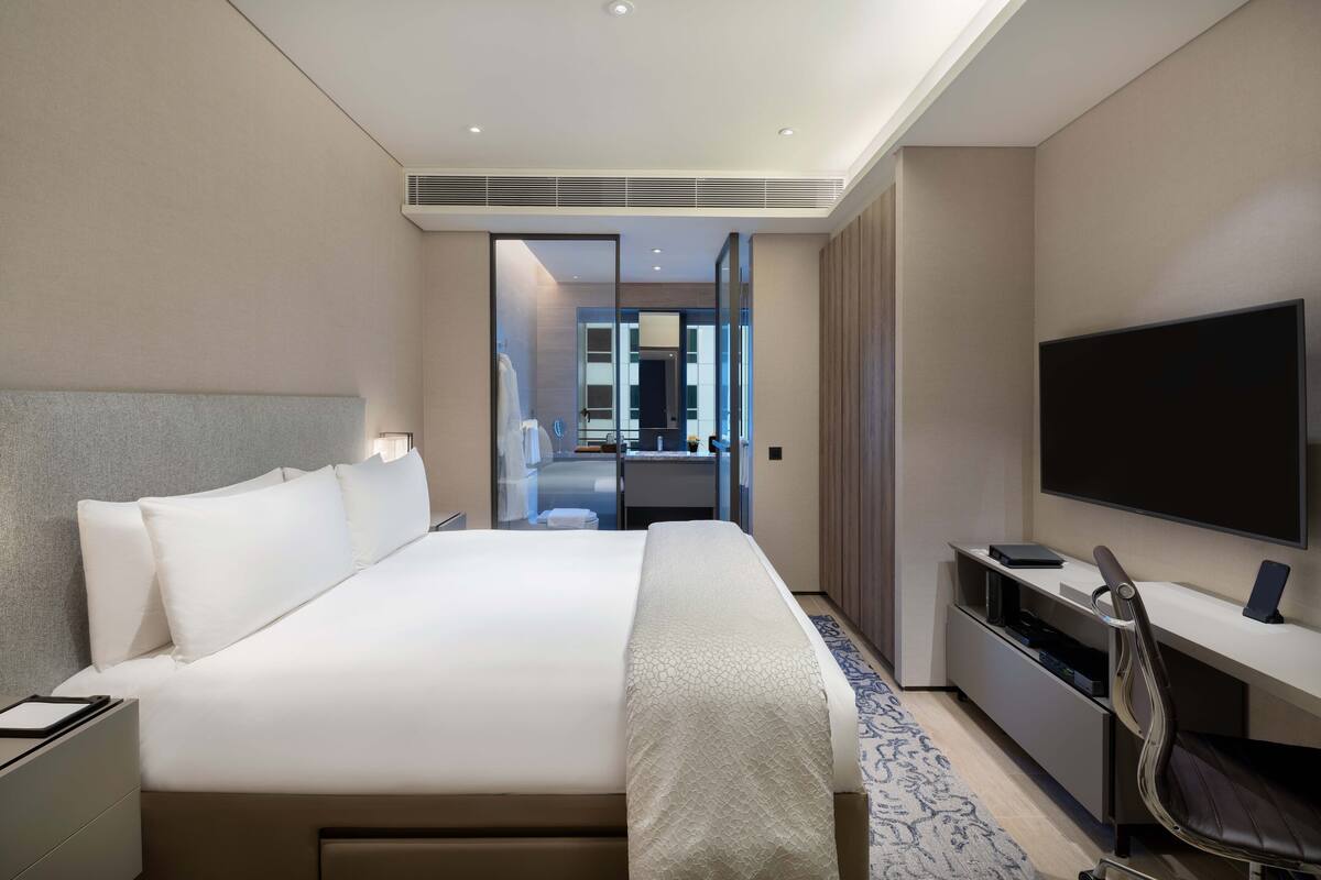 A hotel room with a large bed, a desk with a flat-screen TV, a chair, and a walk-in closet.
