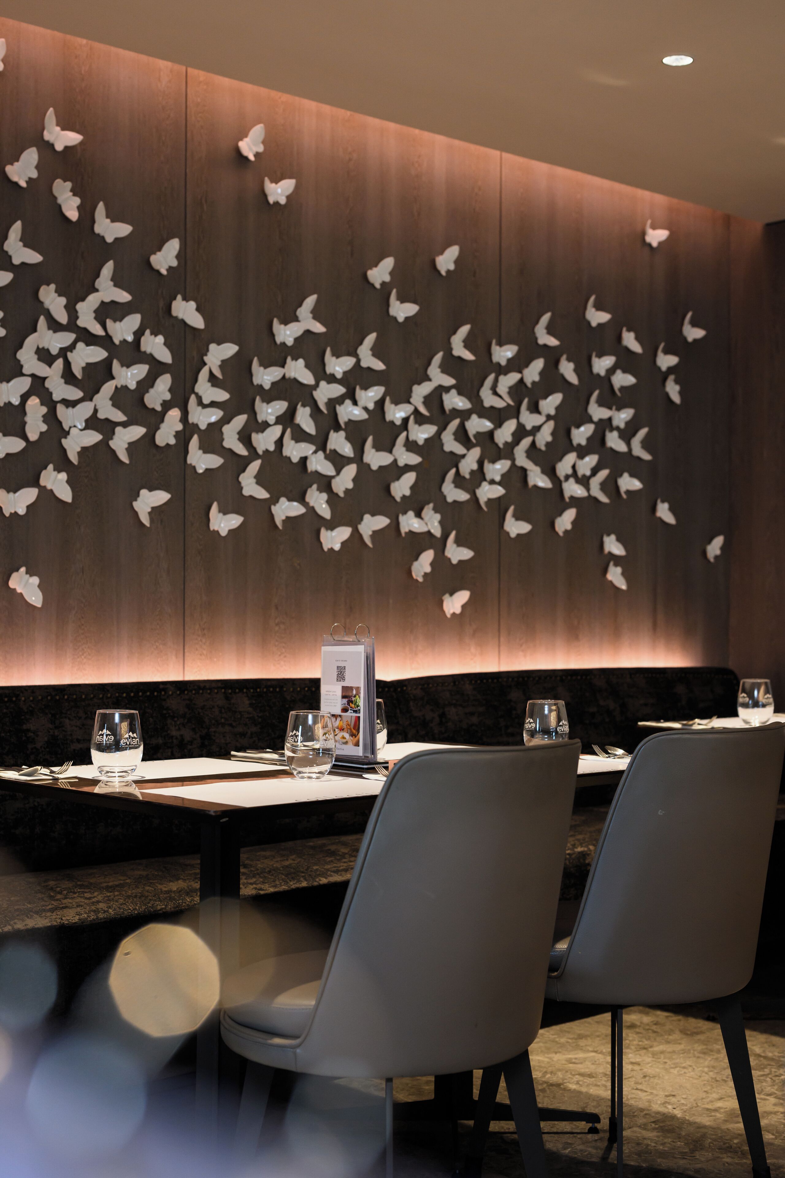 A restaurant interior with a wall of butterfly decorations, a menu stand, and two dining chairs.