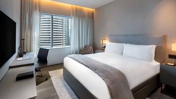Una habitación de hotel moderna con una cama grande, un escritorio, una silla y un televisor.
