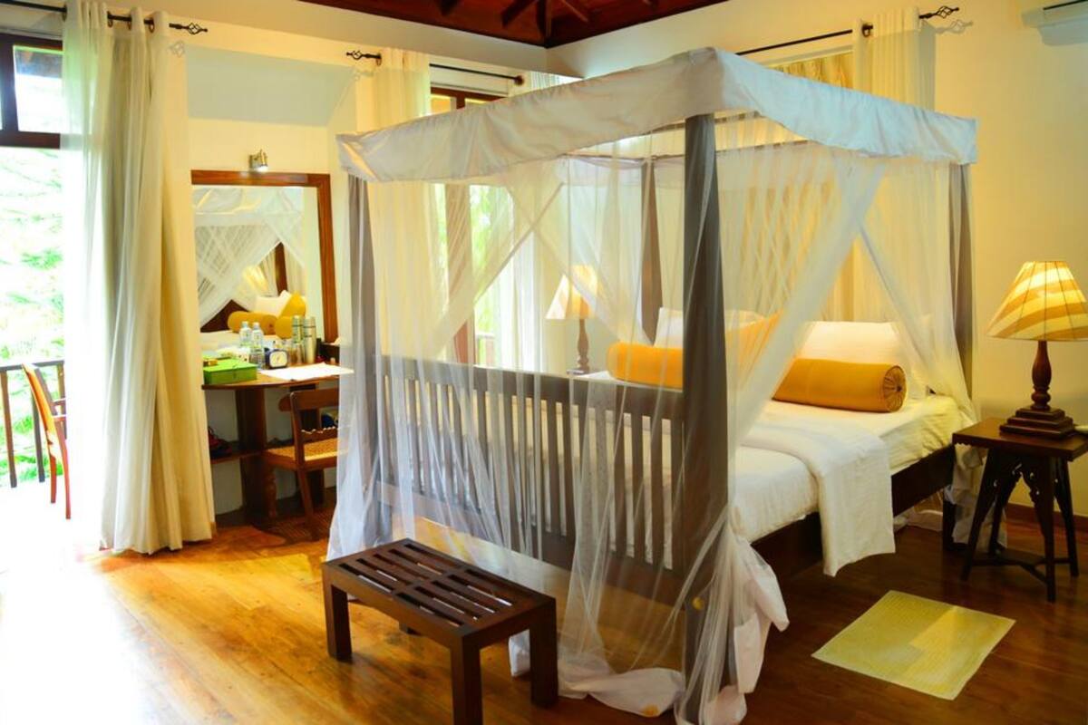 A bedroom with a canopy bed, a desk with a chair, and a bedside table with a lamp.