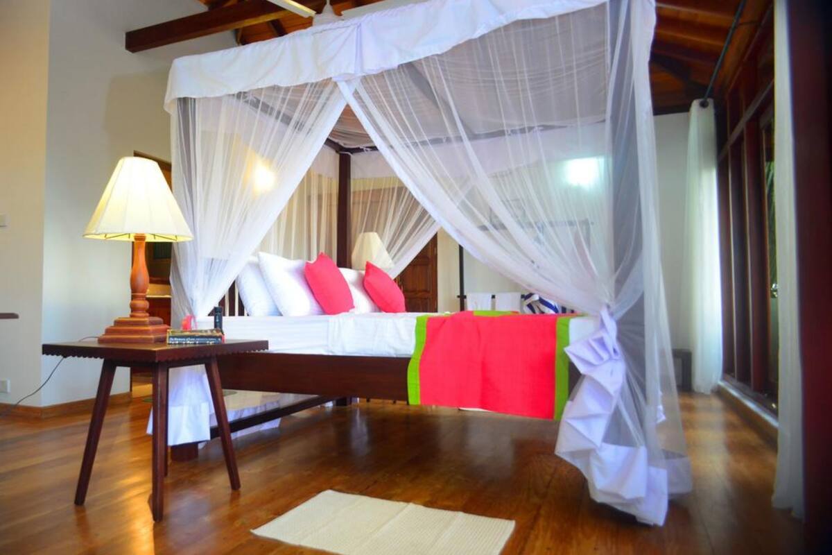 A room with a bed under a canopy, a bedside lamp, and a wooden floor.
