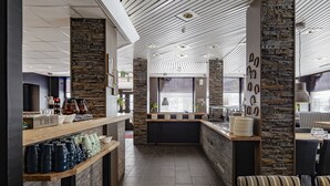 Un intérieur moderne avec un mur d’accent en pierre, un comptoir d’accueil en bois et un espace détente agrémenté de coussins à rayures.