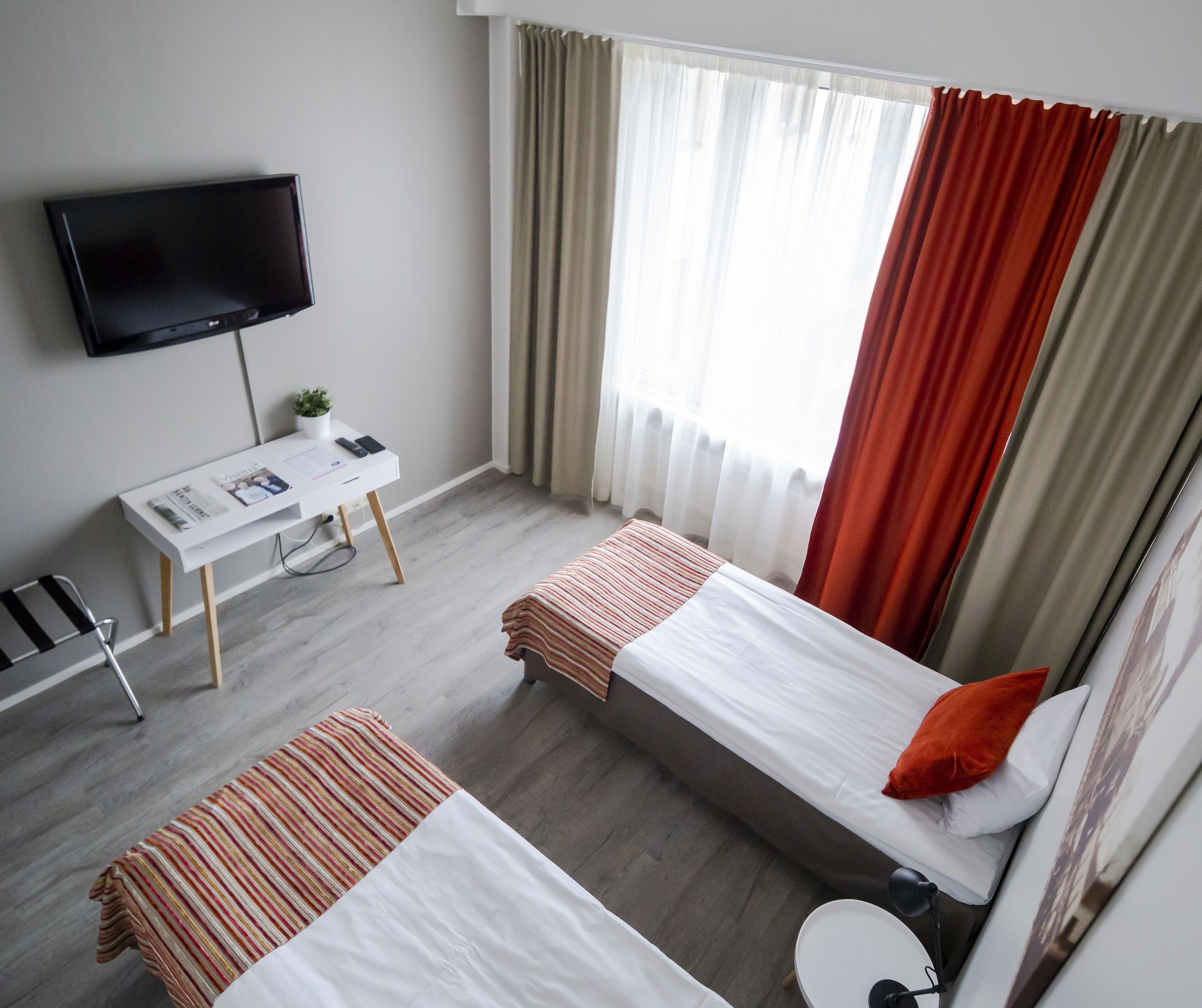 A hotel room with two beds, a desk with a chair, a TV, and a window with curtains.