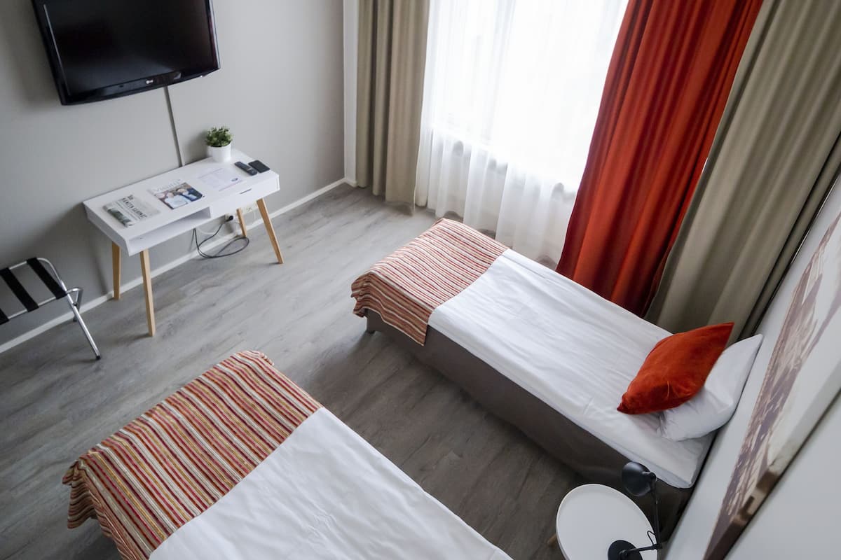 A hotel room with two beds, a desk with a chair, a TV, and a window with curtains.
