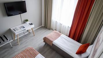 A hotel room with two beds, a desk with a chair, a TV, and a window with curtains.