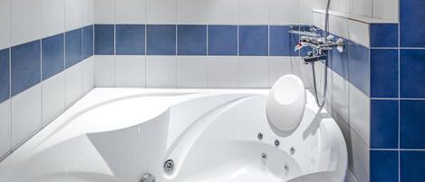 A modern bathroom with a large white bathtub, a handheld showerhead, and a built-in faucet.