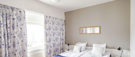 Un dormitorio con una cama doble, una mesita de noche con lámpara, una ventana con cortinas y un radiador.