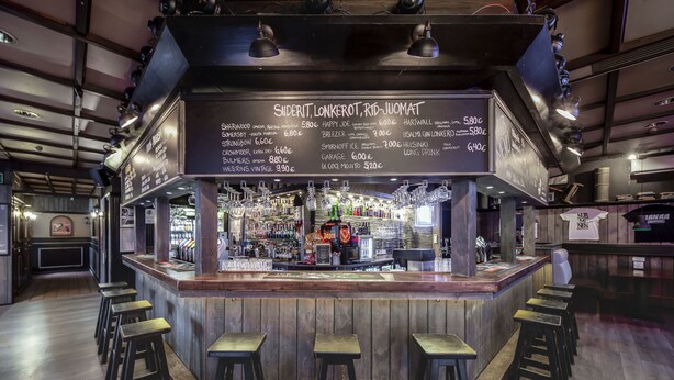 Un espace bar avec des tabourets, un tableau affichant le menu, ainsi qu’une variété de bouteilles et de verres.