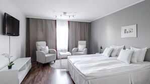 Une chambre d’hôtel moderne avec un grand lit, deux fauteuils, une petite table, un téléviseur et un tableau au mur.