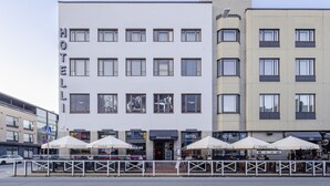 Un hôtel à plusieurs étages, doté d’une terrasse avec des parasols et d’une entrée bien visible.