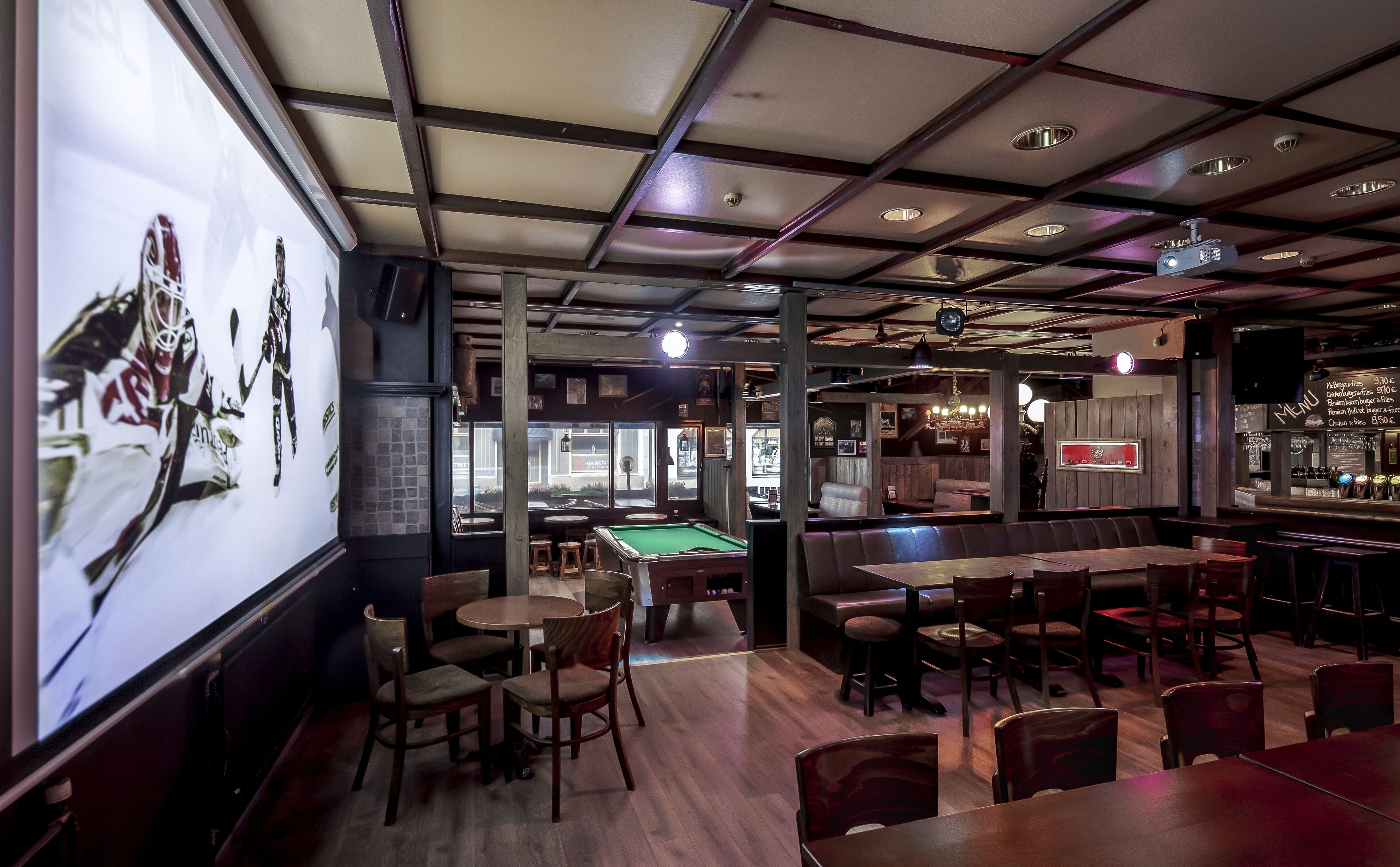 A bar area with pool tables, seating, and a menu board.