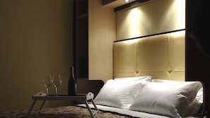 A hotel room with a bed, a bedside table with two wine glasses and a bottle, and a headboard with built-in lighting. - Hotel Alverì (Mestre)
