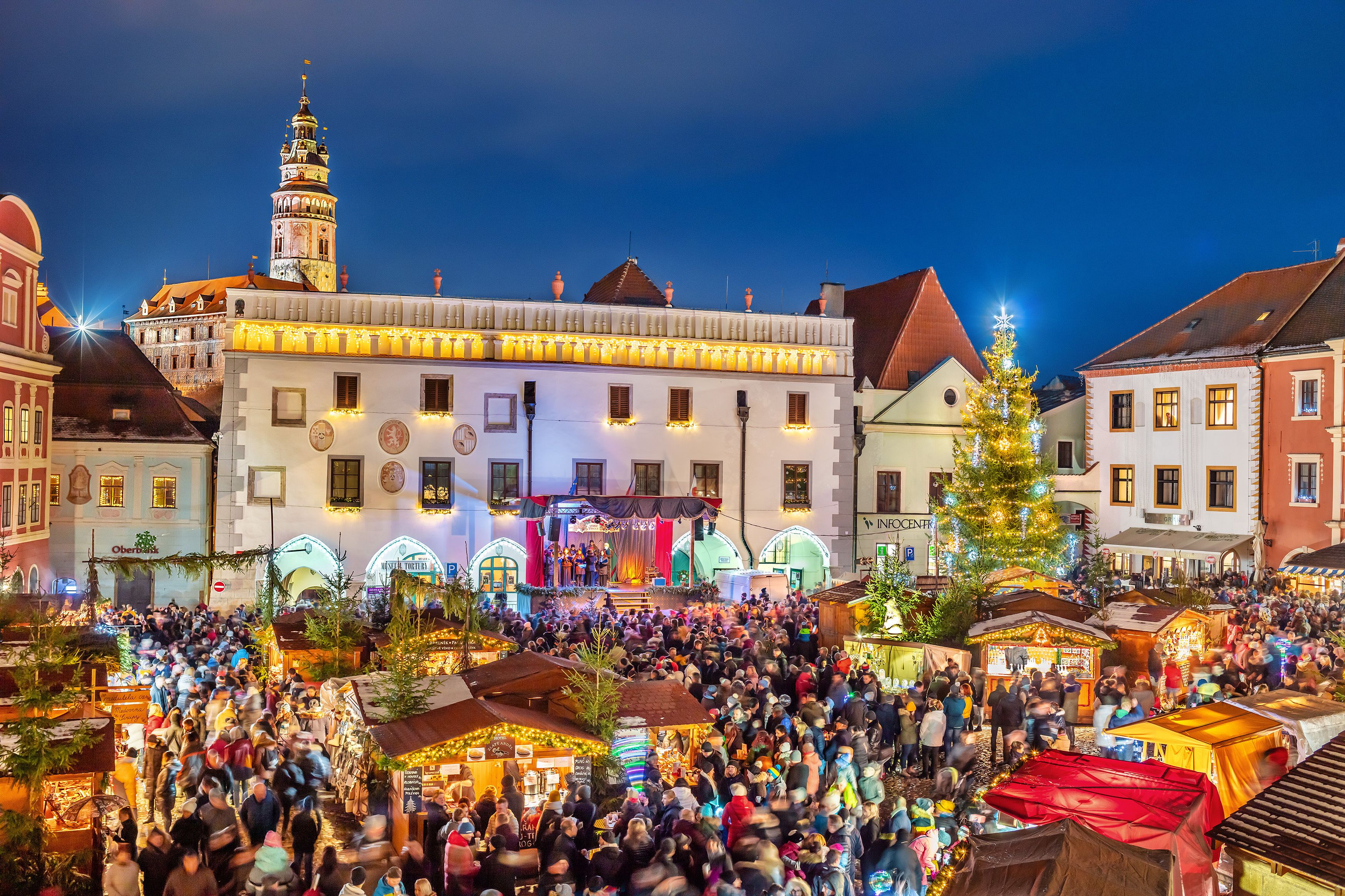 Una vivace piazza di mercato con un edificio importante, dotato di un palco e un grande albero di Natale.