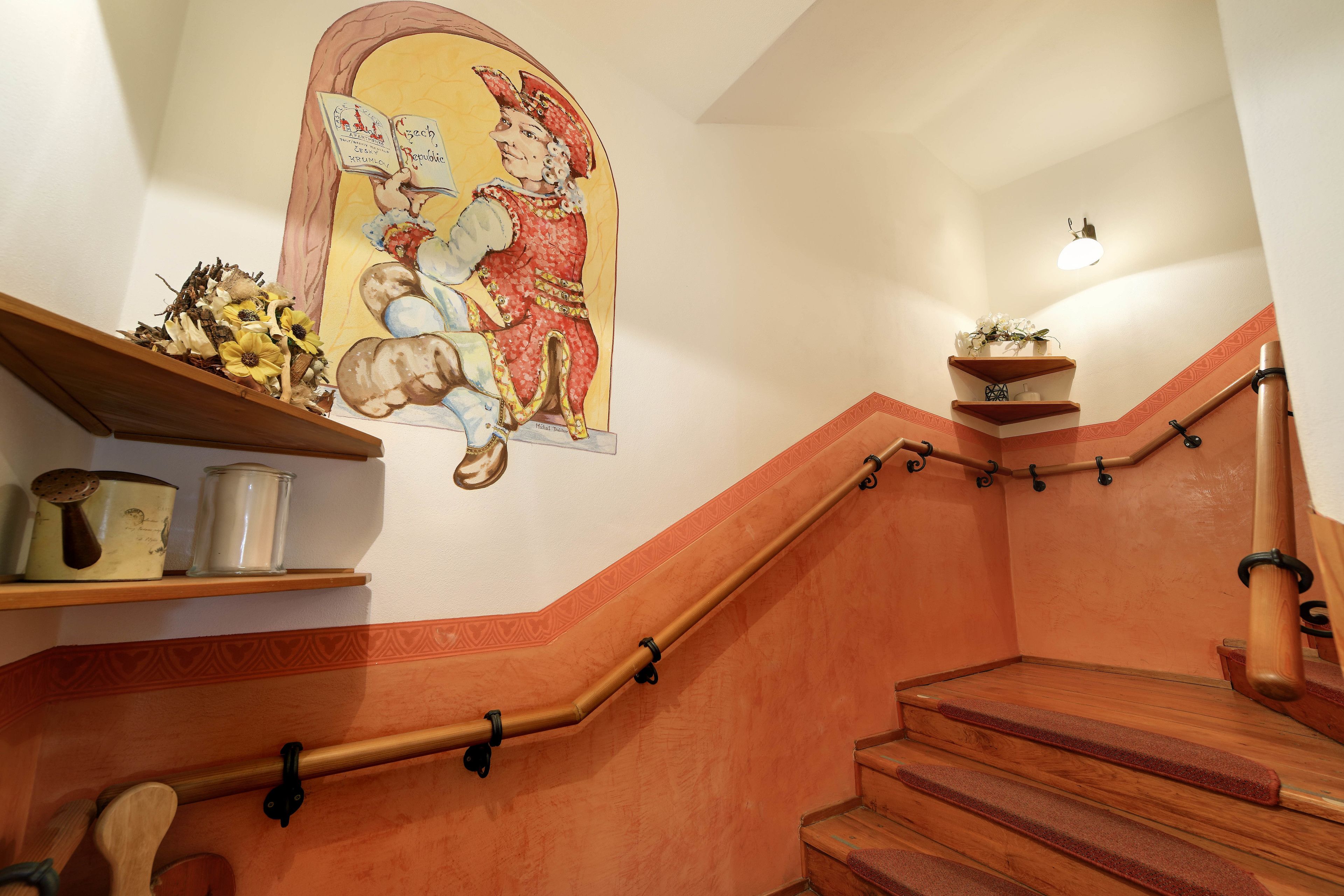 Uma escada de madeira com corrimão, uma parede decorativa com uma pintura e uma prateleira com utensílios de cozinha.