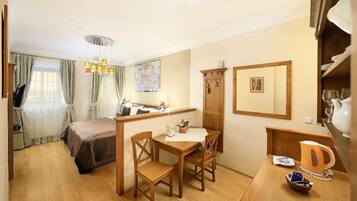 A hotel room with a bed, a dining table with chairs, a kitchen area, and a wooden cabinet.