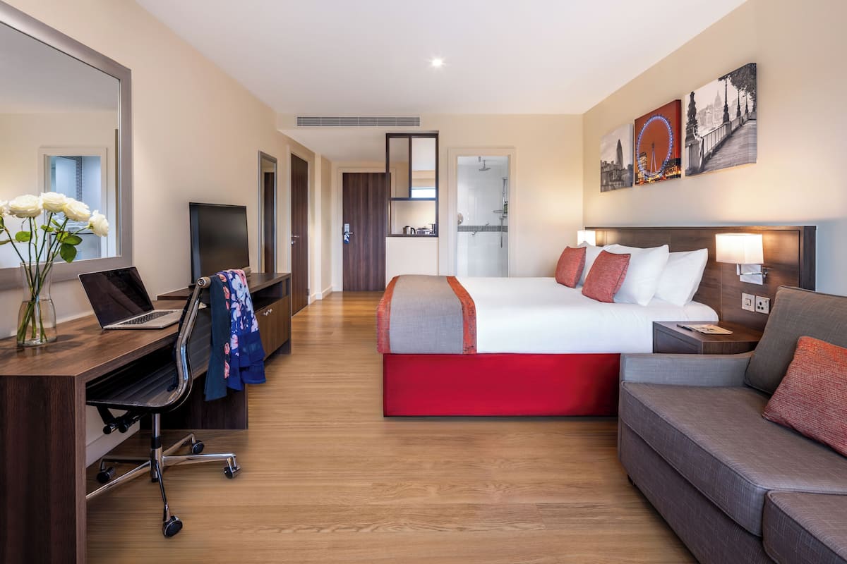 Une chambre d’hôtel équipée d’un lit, d’un bureau, d’une chaise, d’un canapé, d’une télévision et d’œuvres d’art accrochées aux murs.