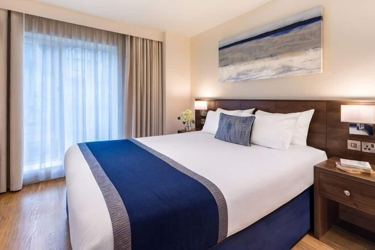 Une chambre d’hôtel avec un grand lit, une table de chevet, une lampe et un tableau au mur.
