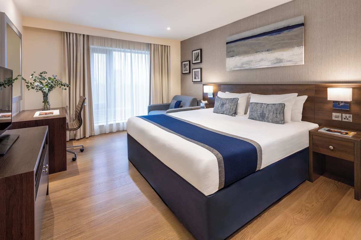 Une chambre d’hôtel avec un grand lit, un bureau, une chaise, une lampe et un tableau au mur.