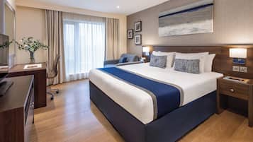 A hotel room with a large bed, a desk, a chair, a lamp, and a painting on the wall.